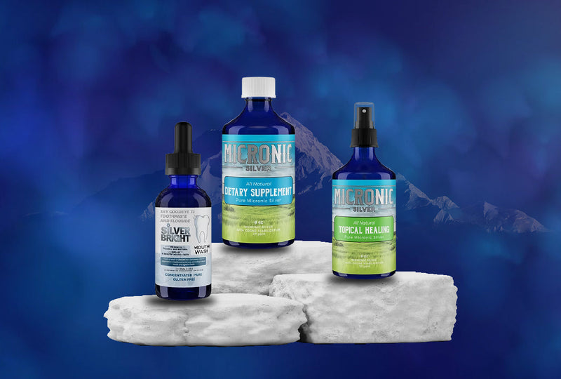 Three blue bottles of health supplements labeled Silver Bright and Micronic Silver on white stone with blue mountain background.