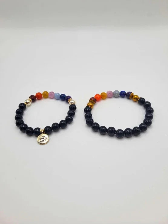 Pair of chakra bead bracelets with black stones and colorful accents on white background