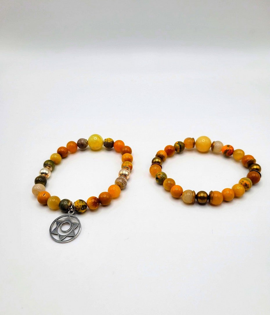Pair of orange and yellow gemstone beaded spiritual bracelets, one with a metal charm, on white background