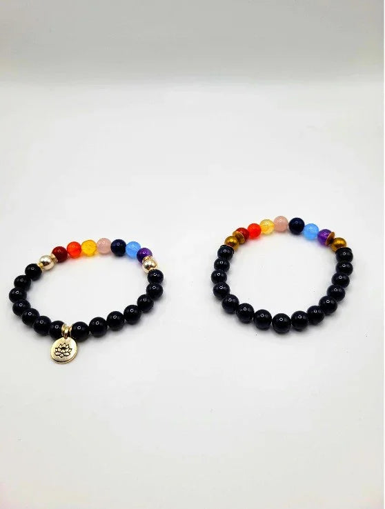 Two chakra bead bracelets with black and colorful stones on white background, one with lotus charm