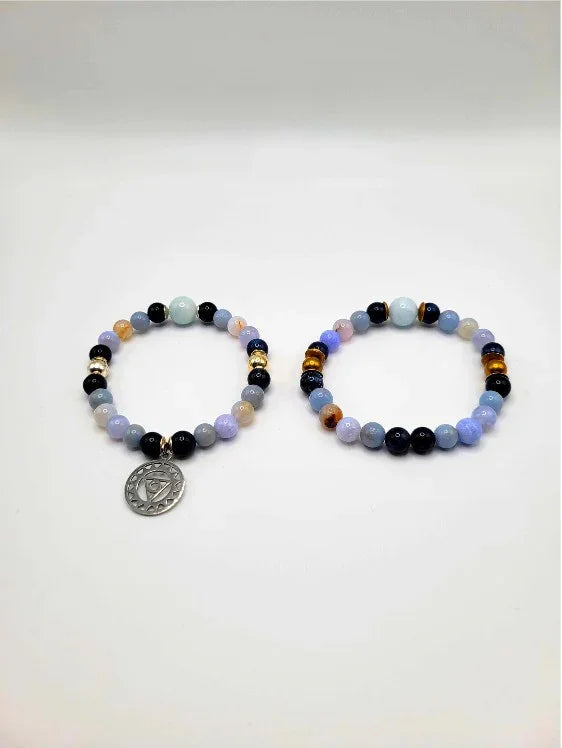 Pair of beaded spiritual bracelets with gemstone beads and silver charm on white background