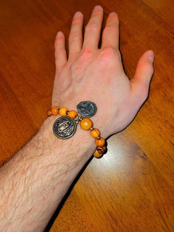 Hand wearing a wooden beaded spiritual bracelet with religious medallion charms on a wooden table