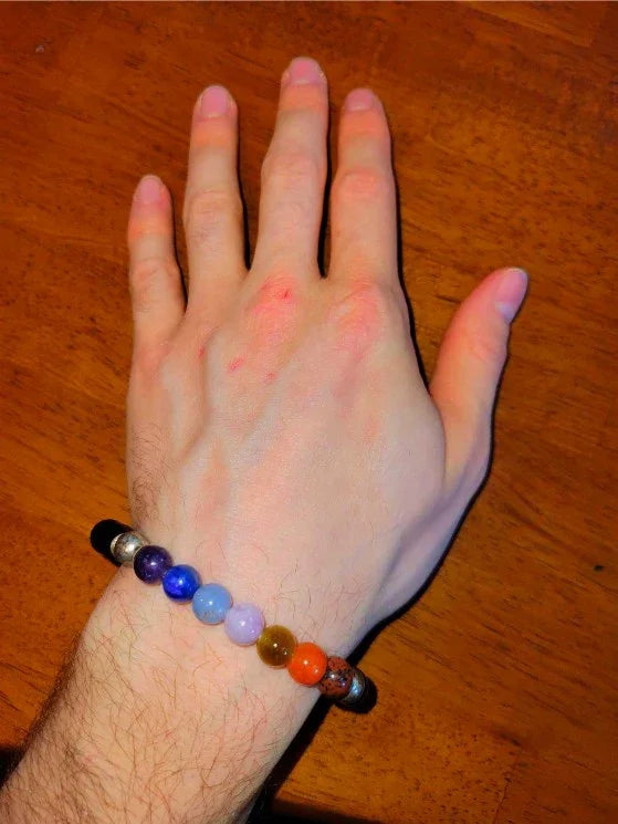 Hand wearing a colorful chakra stone beaded bracelet on wooden surface
