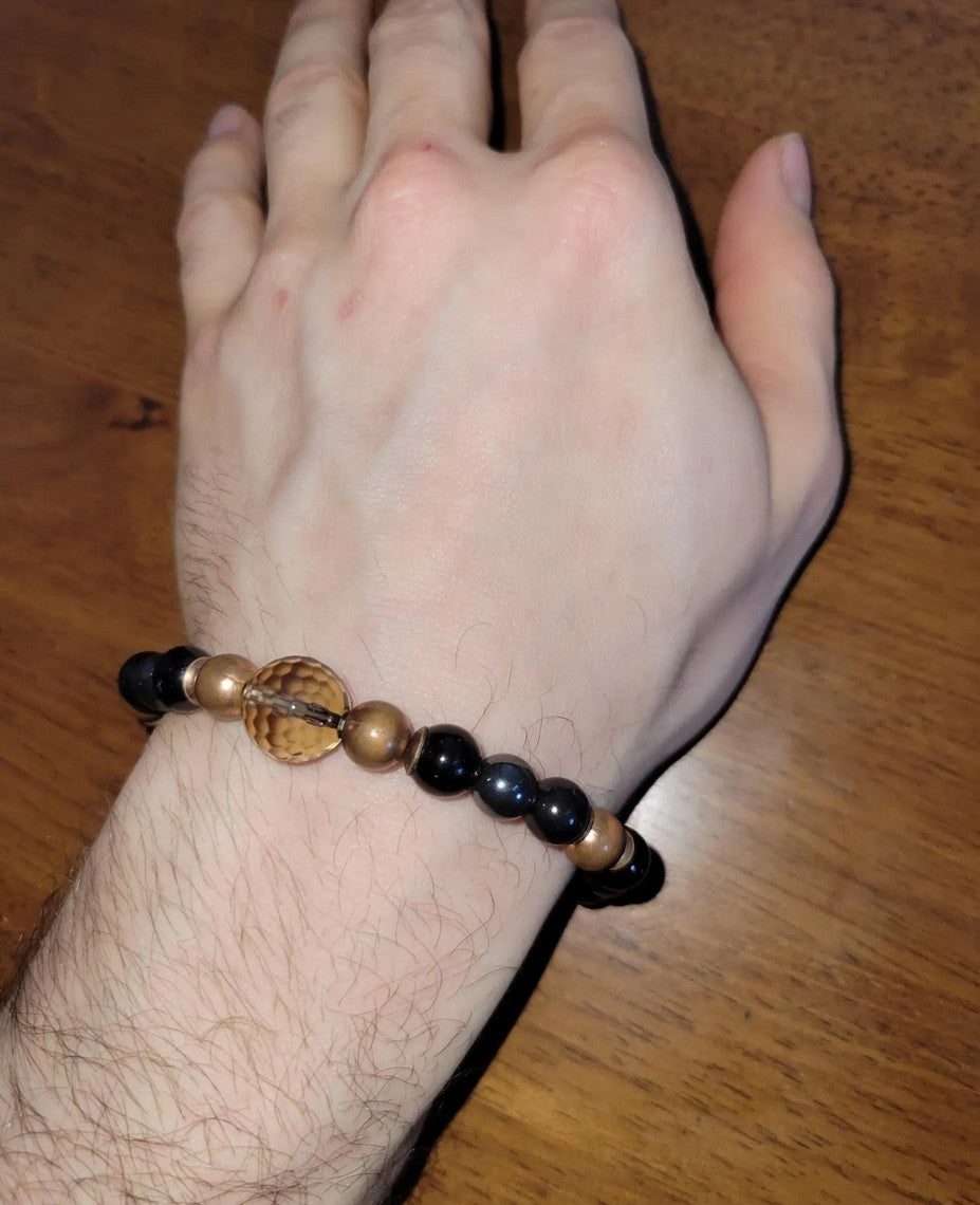 Hand wearing a beaded spiritual bracelet with black and wooden beads on wooden table