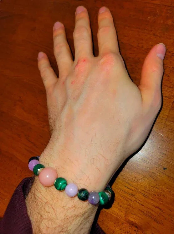 Hand wearing a colorful gemstone beaded bracelet on a wooden surface