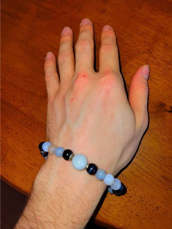 Hand wearing a beaded spiritual bracelet with blue and black round stones on a wooden table
