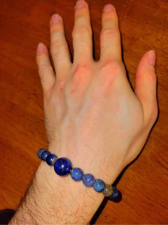 Hand wearing blue gemstone beaded bracelet on wooden table, spiritual jewelry