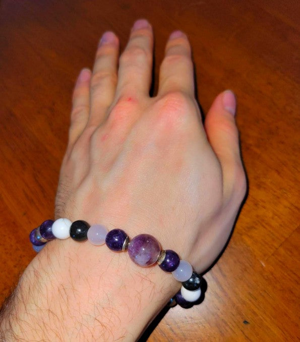 Hand wearing a purple, white, and black beaded spiritual bracelet on wooden table