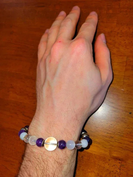 Hand wearing a beaded spiritual bracelet with amethyst and clear round beads on wood surface