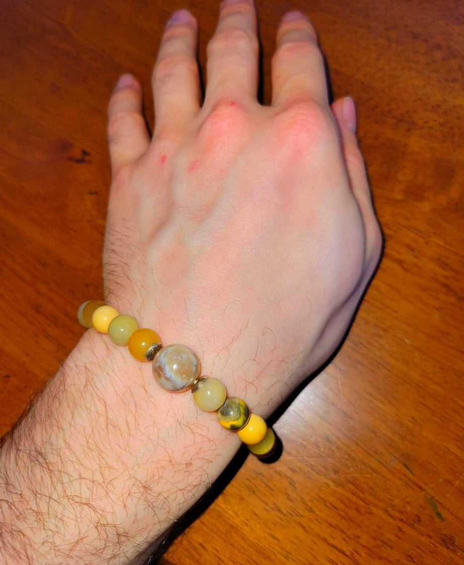 Hand wearing a yellow and brown beaded spiritual bracelet on a wooden table
