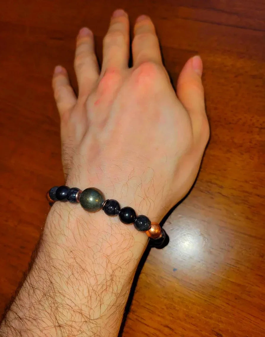 Hand wearing black and copper beaded spiritual bracelet on wooden table