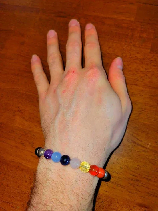 Hand wearing a colorful chakra bead spiritual bracelet on wood surface
