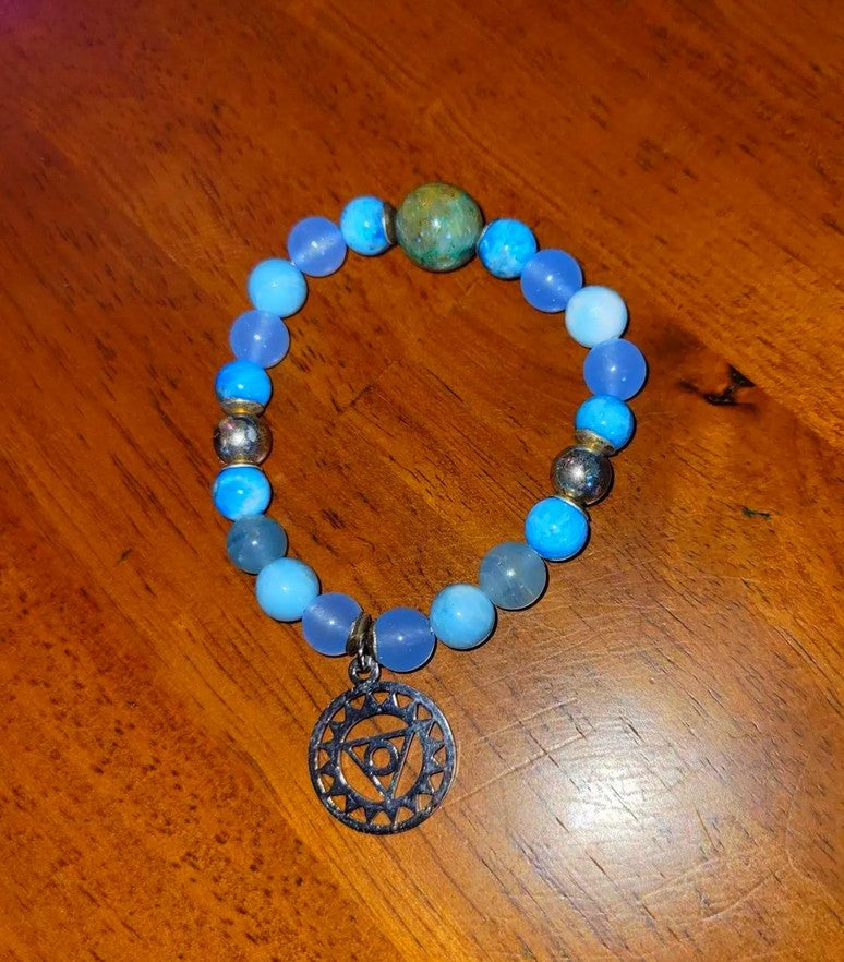 Blue beaded chakra bracelet with silver spiritual charm on wood surface