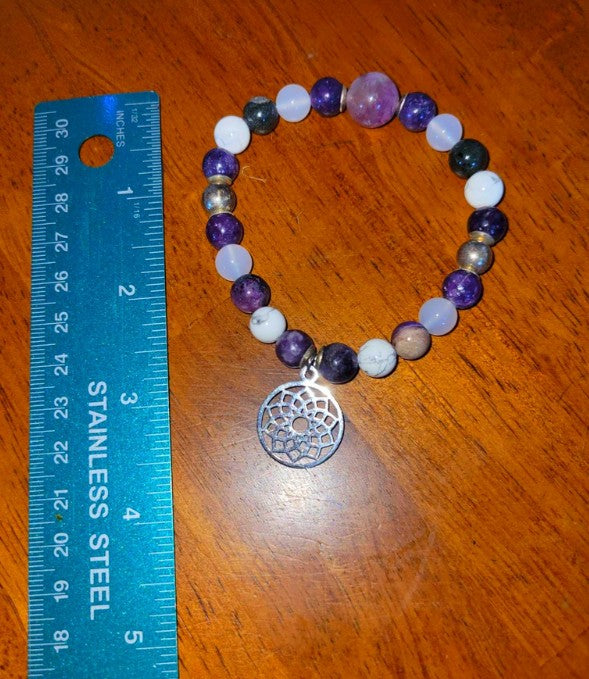 Beaded spiritual bracelet with dreamcatcher charm and colorful stones beside ruler on wood table