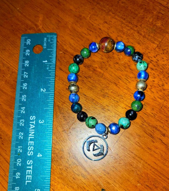 Colorful beaded spiritual bracelet with metal charm beside ruler on wooden surface