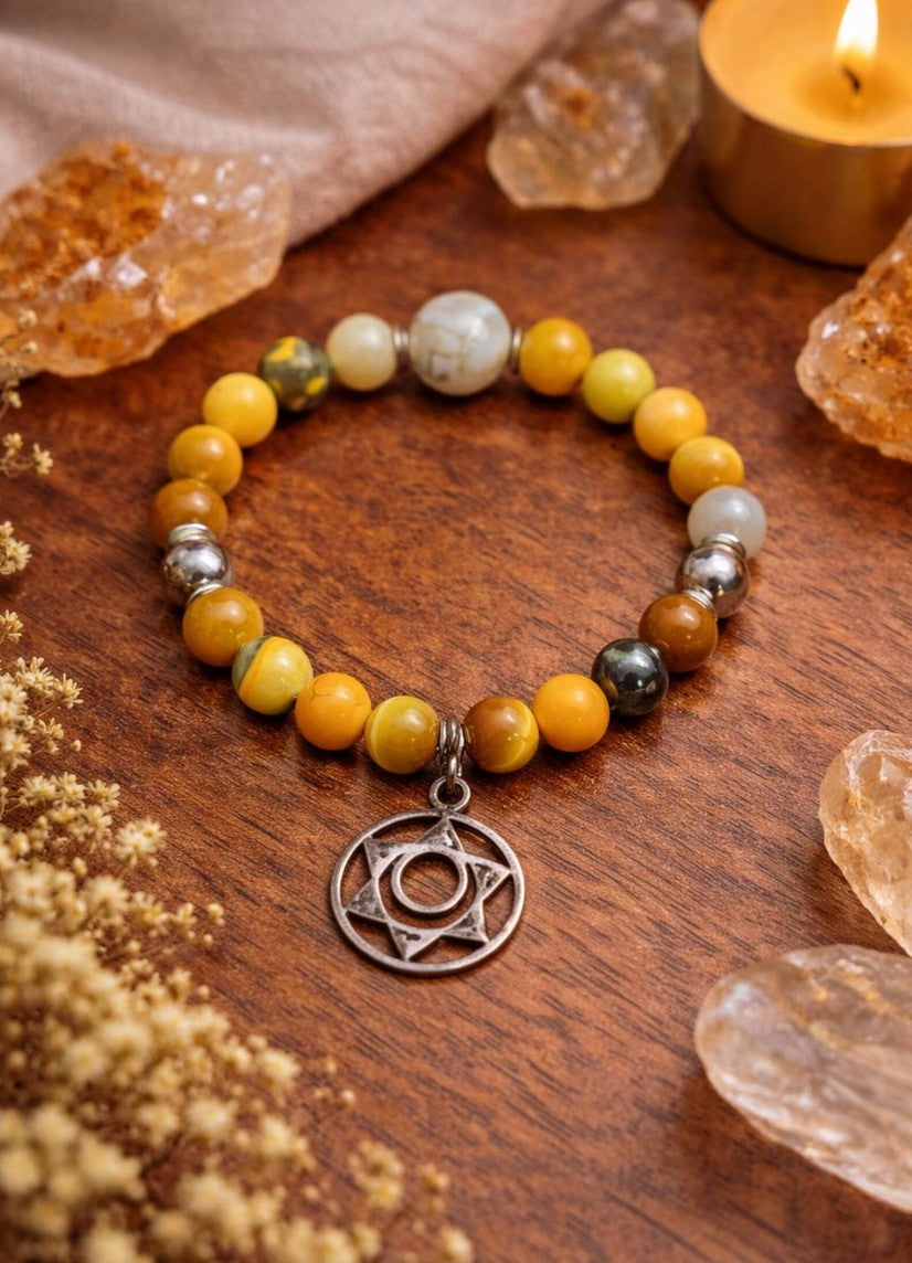 Yellow beaded spiritual bracelet with metal pendant on wood, crystals and candle nearby
