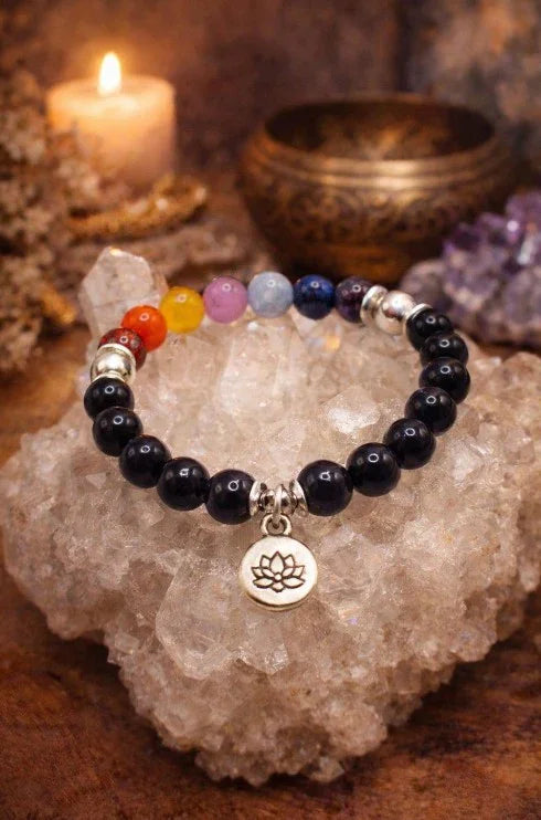 Chakra gemstone bracelet with lotus charm on crystal, surrounded by candle and amethyst decor