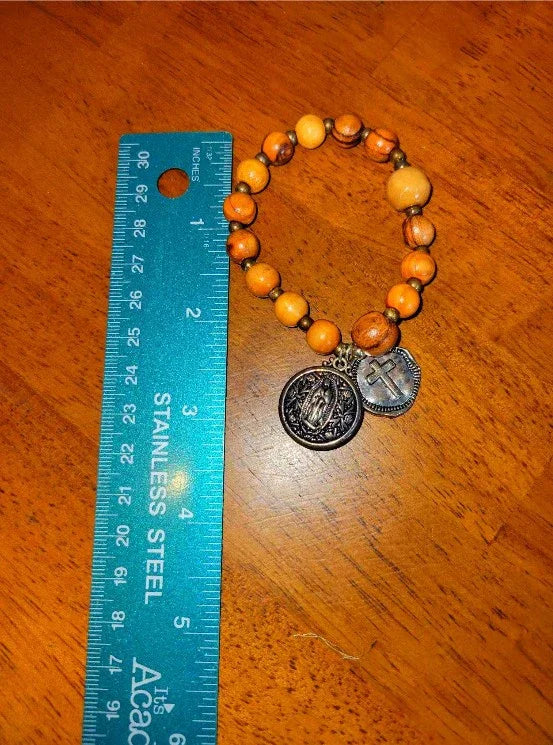 Wooden beaded spiritual bracelet with two metal charms beside a blue ruler on a wooden table.