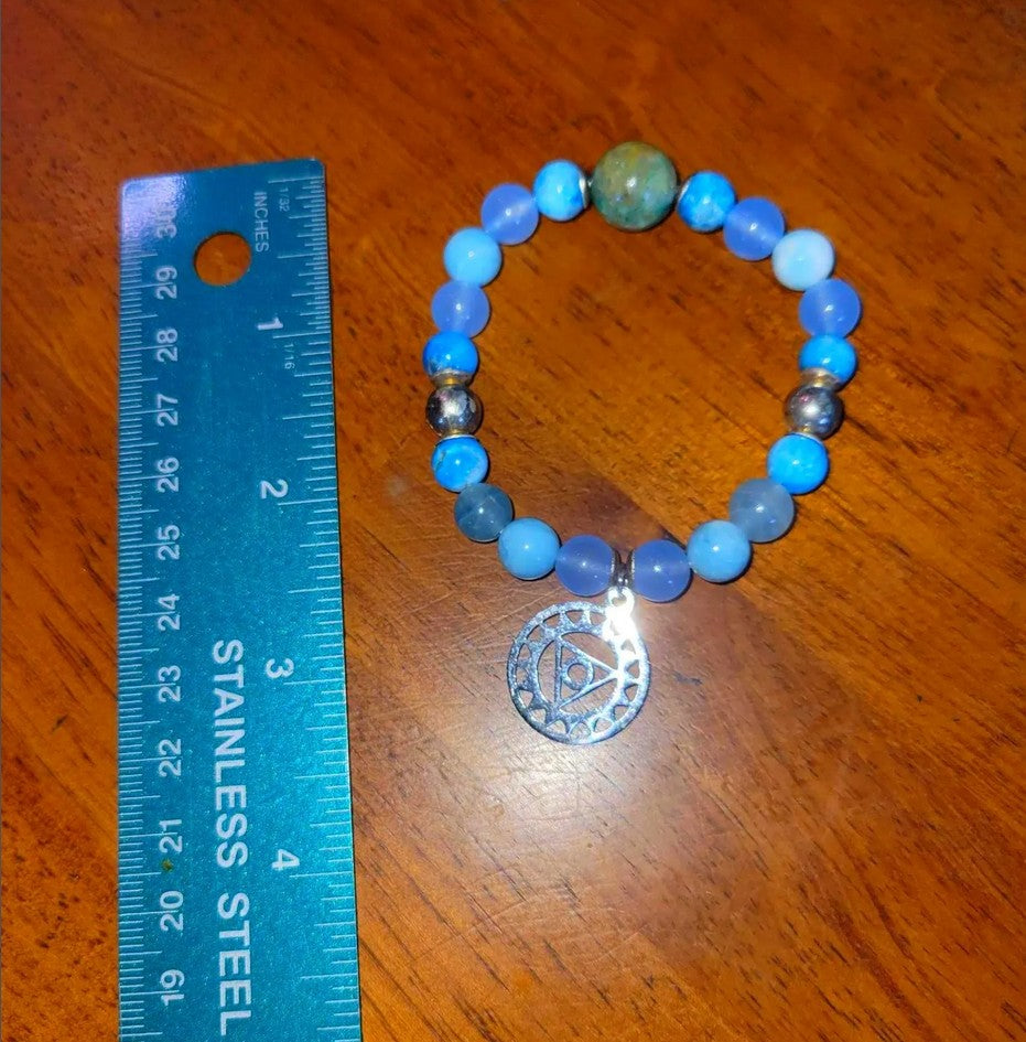 Blue beaded spiritual bracelet with silver charm next to stainless steel ruler on wood surface