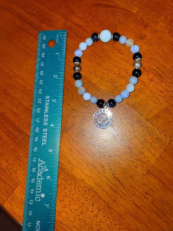 Beaded spiritual bracelet with charm, next to blue ruler on wooden table