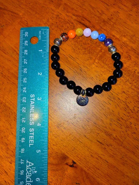 Black bead chakra bracelet with charm next to stainless steel ruler on wood surface