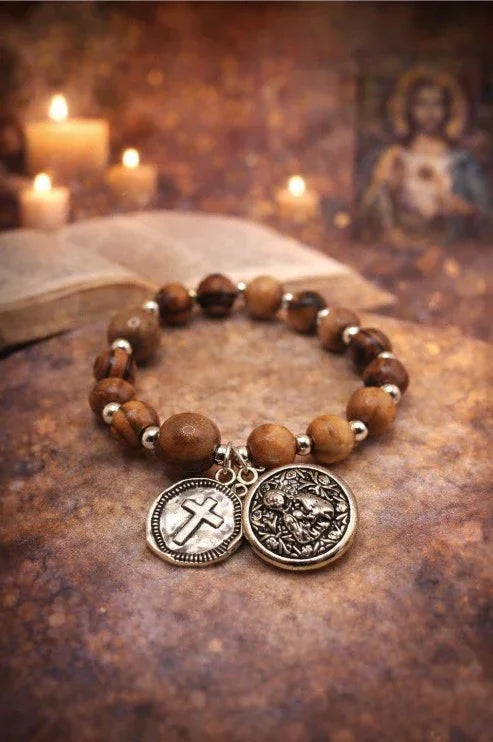 Wooden beaded spiritual bracelet with metal cross and lion charms, candles and open book in background