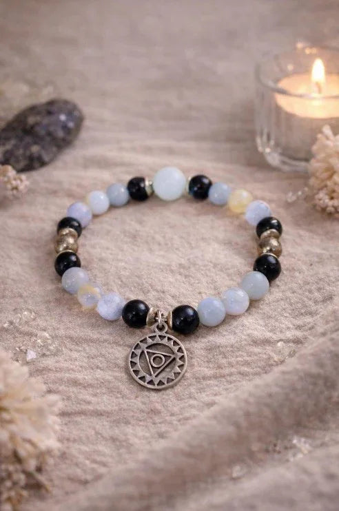 Beaded spiritual bracelet with gemstone beads and silver pendant, displayed on textured fabric with candle.