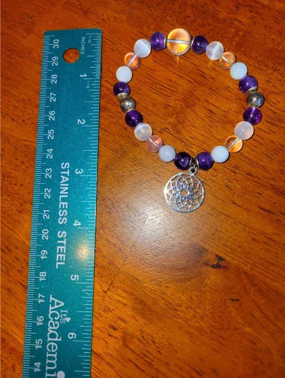 Beaded spiritual bracelet with dreamcatcher charm beside a ruler on wood surface