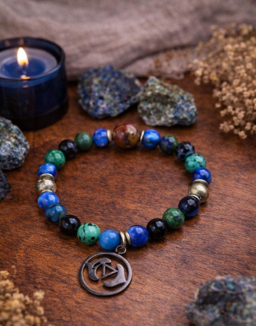 Colorful beaded spiritual bracelet with metallic charm on wooden table, candle and stones nearby