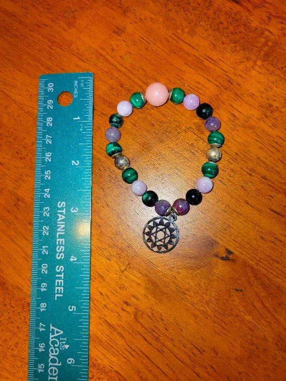 Colorful gemstone beaded spiritual bracelet with mandala charm next to a ruler on wood table