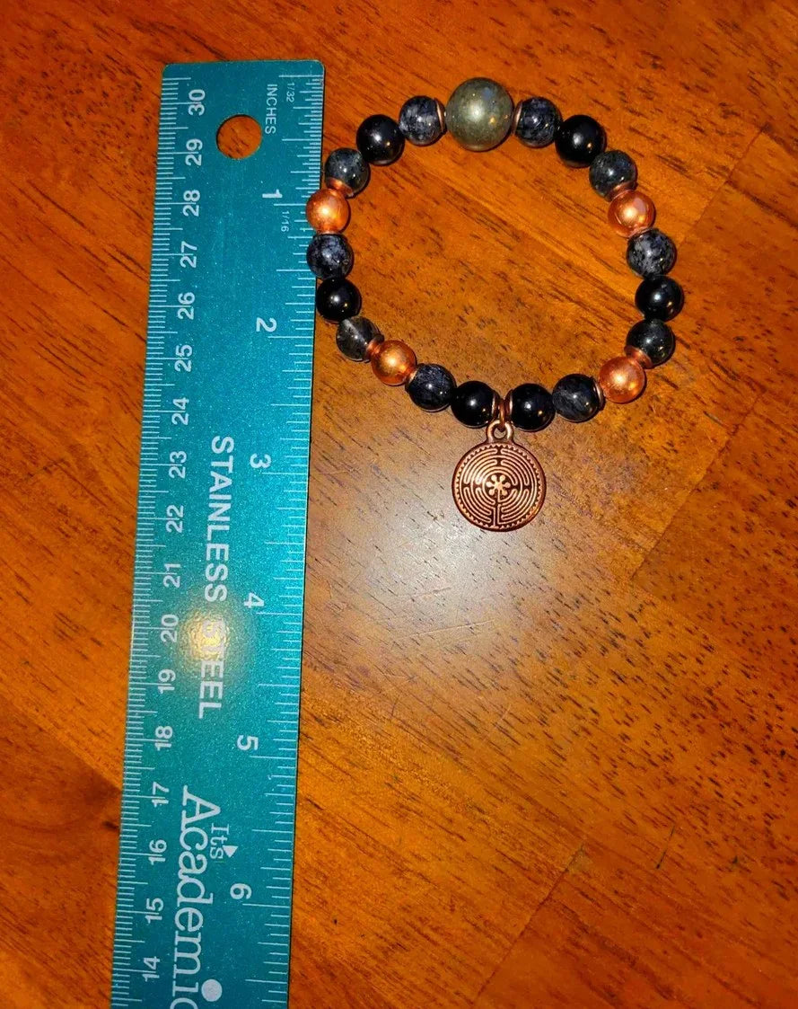 Beaded gemstone bracelet with bronze charm beside a ruler on wooden surface