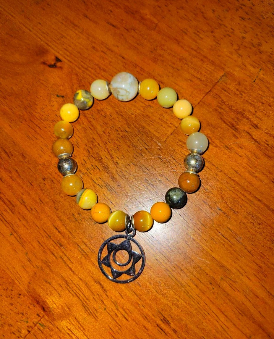 Yellow and silver beaded spiritual bracelet with a metal geometric charm on wooden surface