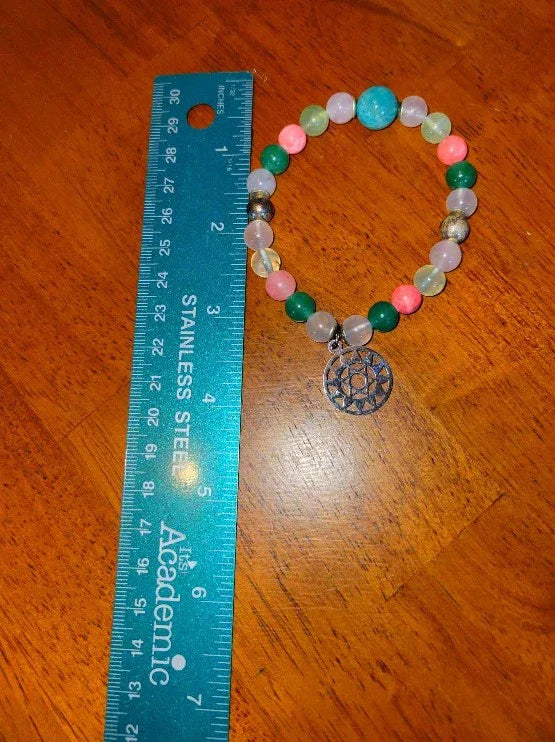 Colorful beaded spiritual bracelet with tree of life charm beside blue ruler on wood table
