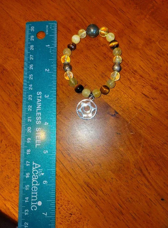 Beaded gemstone spiritual bracelet with silver charm next to ruler on wood surface