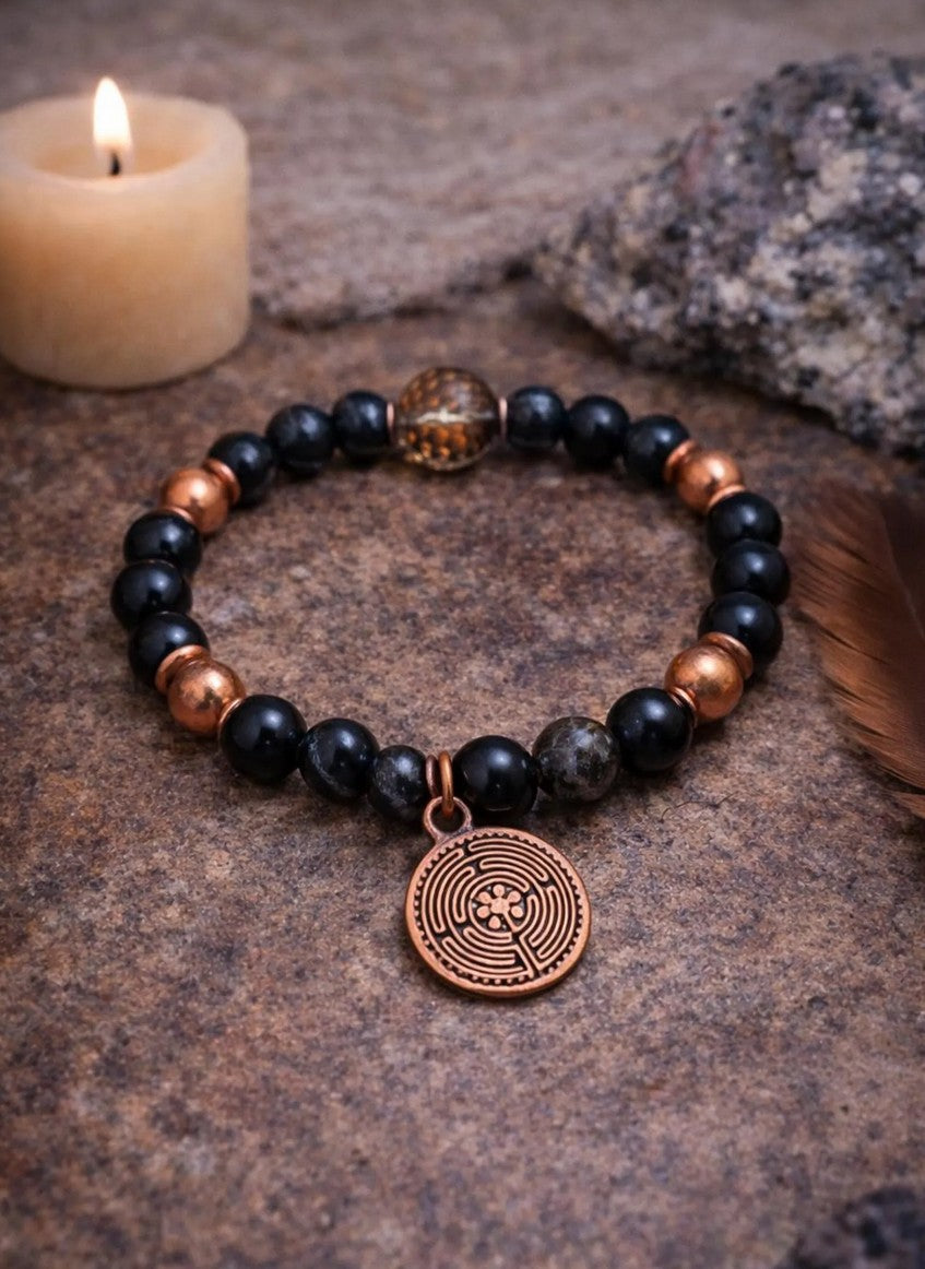 Black bead spiritual bracelet with copper charm on stone, candle and feather nearby