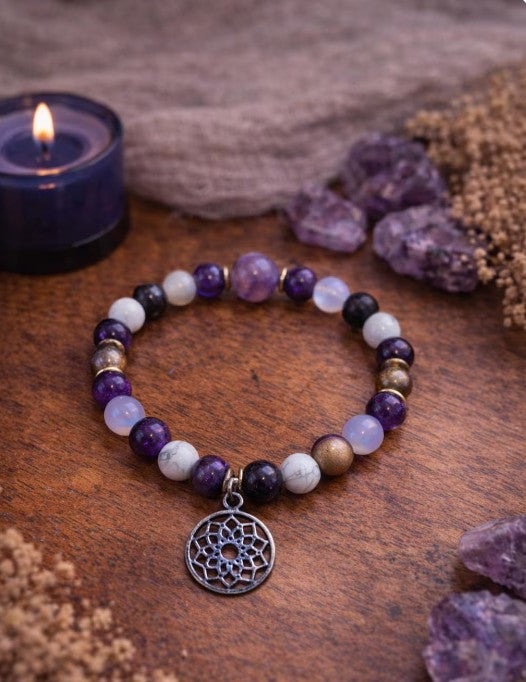 Amethyst beaded spiritual bracelet with dreamcatcher charm on wooden table, candle and crystals nearby