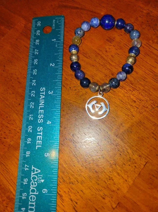 Blue gemstone bead bracelet with metallic charm next to stainless steel ruler on wood surface