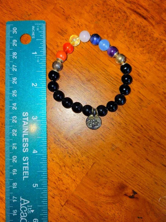 Multicolor chakra bead bracelet with lotus charm next to a teal stainless steel ruler on wood.