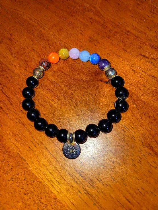 Chakra spiritual bracelet with black beads, colorful stones, and lotus charm on wooden surface