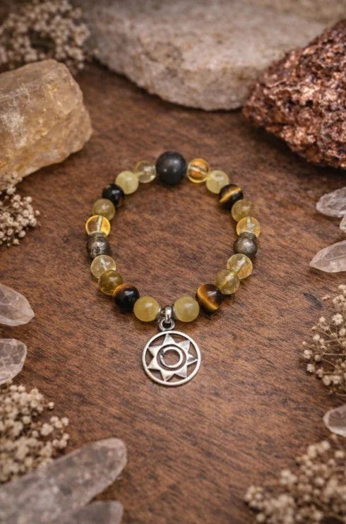 Yellow and black gemstone beaded bracelet with silver spiritual charm on wooden surface with crystals