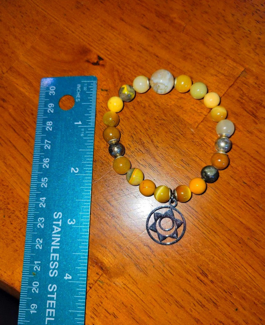 Yellow and silver beaded spiritual bracelet with star pendant next to a ruler on wooden surface