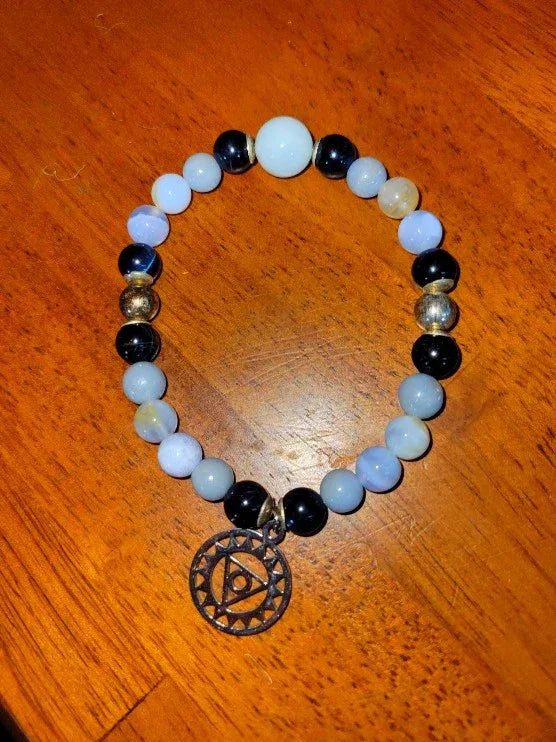 Beaded spiritual bracelet with blue, black, and metallic beads and an eye charm on wood surface.