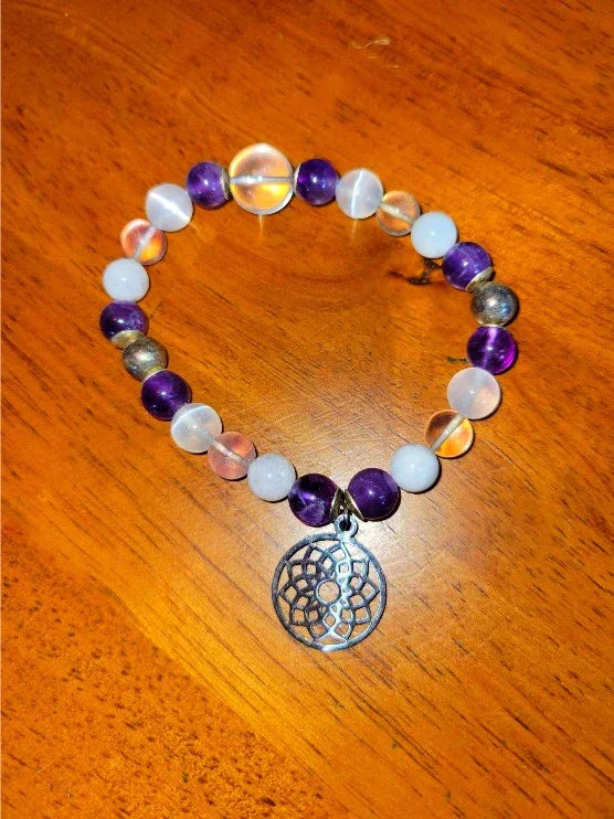 Beaded spiritual bracelet with amethyst, clear and metallic beads, dreamcatcher charm on wood surface