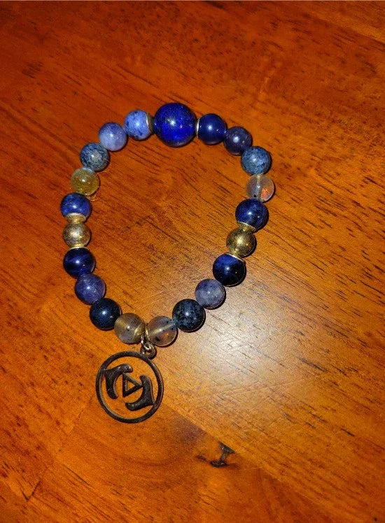 Blue and gold beaded spiritual bracelet with metal charm on wooden surface