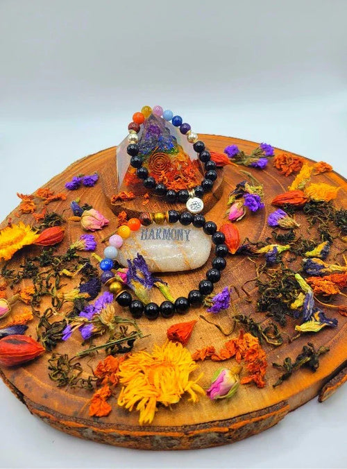 Chakra beaded bracelets on wooden tray with dried flowers, gemstone, and 'Harmony' stone