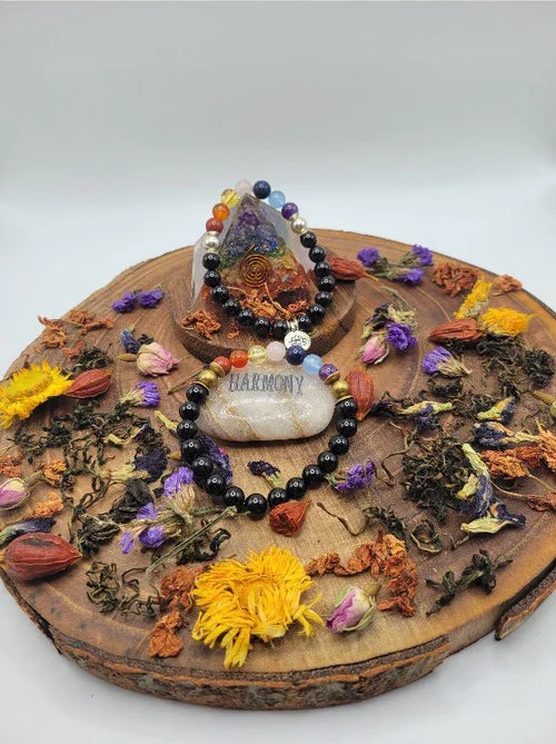 Chakra crystal beaded bracelets on a wooden tray with dried flowers, gemstone, and 'harmony' stone.