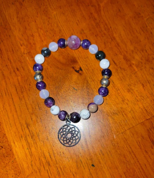 Purple and white beaded spiritual bracelet with dreamcatcher charm on wooden surface