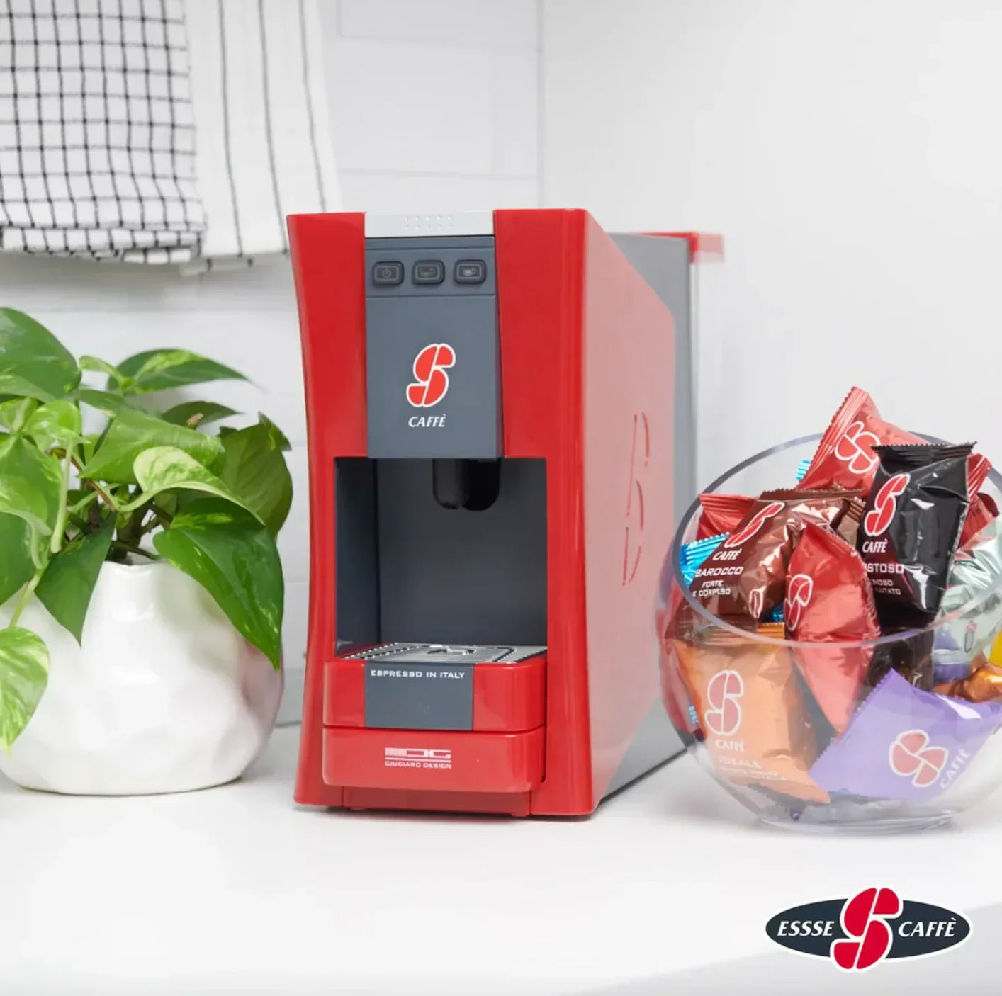 Red espresso coffee machine with assorted Essse Caffè pods on a white kitchen counter